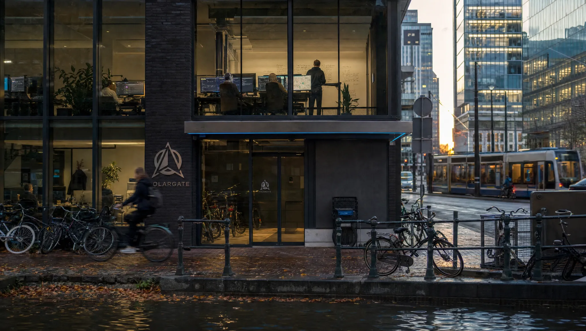 A street in Amsterdam at dusk, bicycles along the railing and lit office floors behind the glass.
